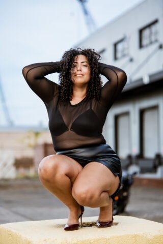 Reclaiming Her Power: An Industrial Boudoir & Motorcycle Session Rawle Jackman Photography NJ Boudoir & Portrait Photographer | Rawle Jackman Boudoir photography on concrete block — woman crouching in sheer top and leather skirt against industrial warehouse backdrop, NJ boudoir photographer.