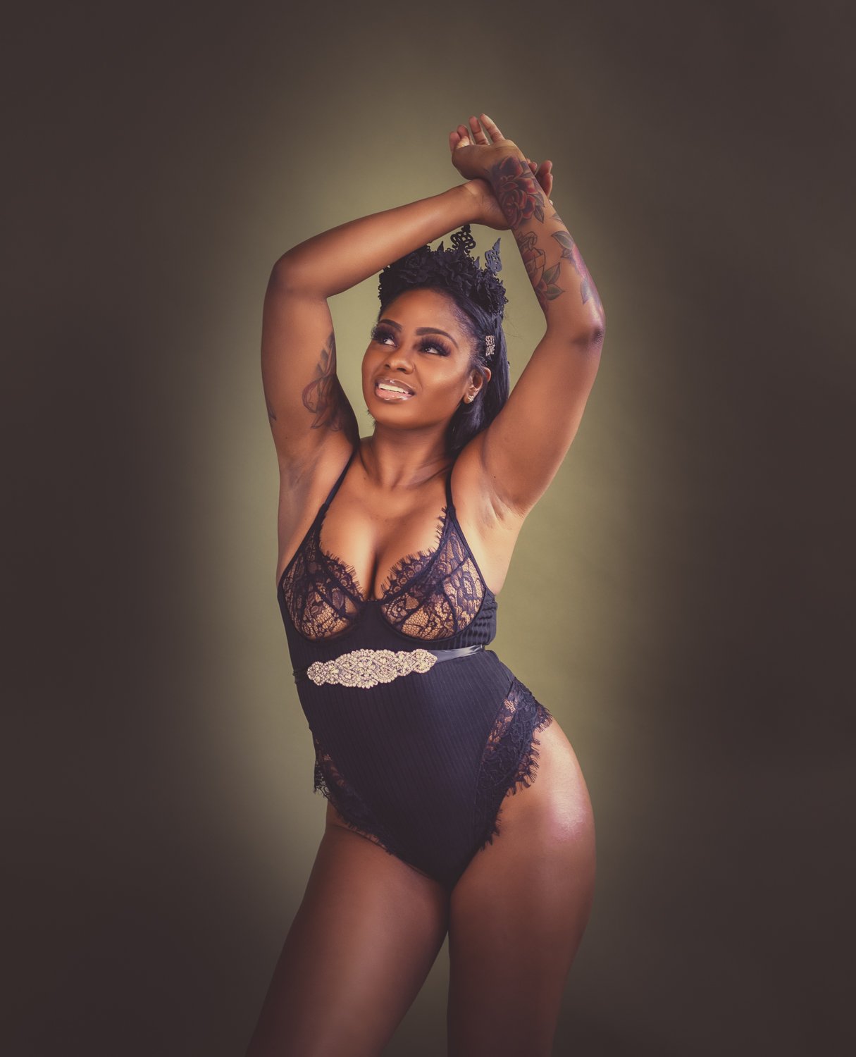 boudior portait of a woman with her arms raised and smiling while wearing lingerie