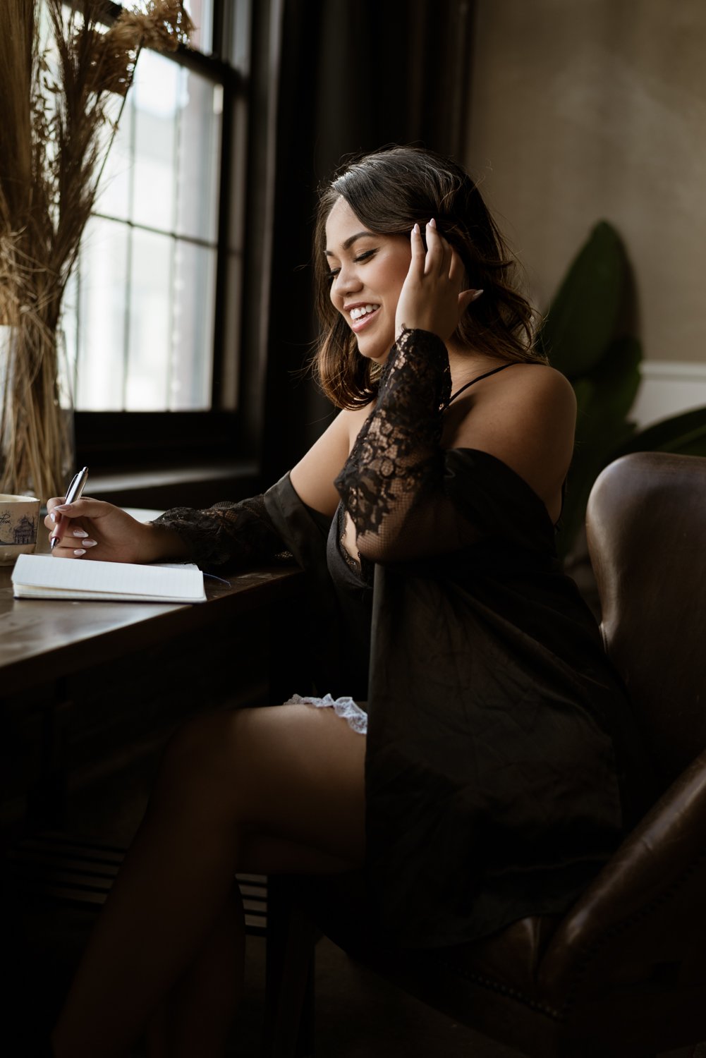 woman sitting on a chair reading a book at window in lingerie and smiling